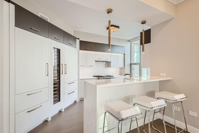 kitchen featuring a peninsula, wood finished floors, light countertops, a kitchen bar, and decorative light fixtures