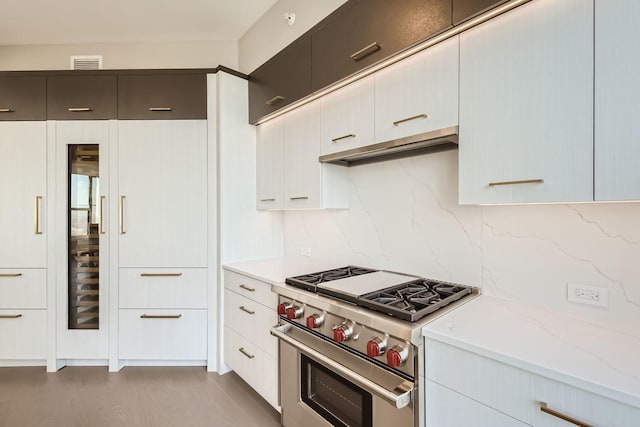 kitchen with tasteful backsplash, visible vents, white cabinets, high end range, and under cabinet range hood