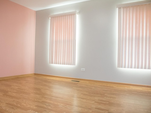 unfurnished room featuring light wood-type flooring, visible vents, and baseboards