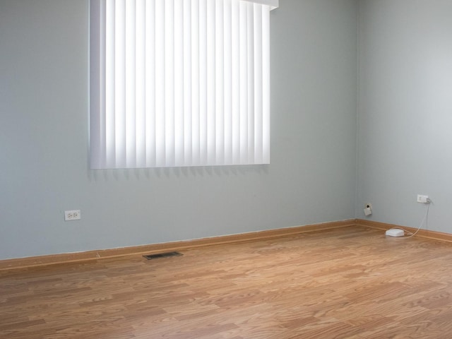 spare room featuring light wood-type flooring, visible vents, and baseboards