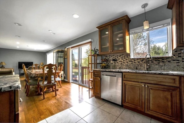 kitchen featuring light stone counters, stainless steel dishwasher, a sink, and glass insert cabinets