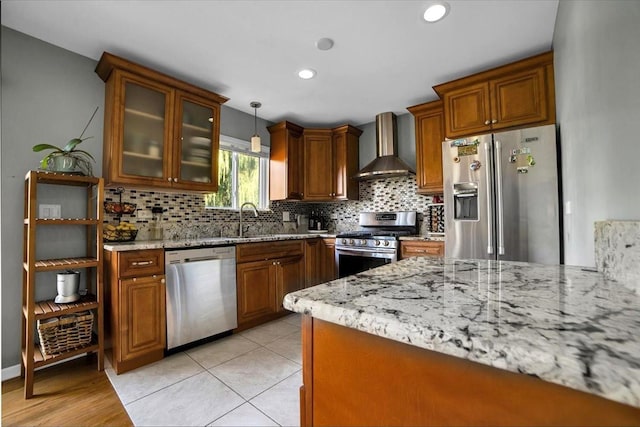 kitchen featuring light stone counters, brown cabinets, appliances with stainless steel finishes, glass insert cabinets, and wall chimney exhaust hood