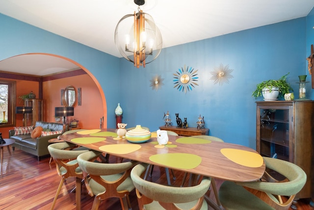 dining area featuring arched walkways, an inviting chandelier, and wood finished floors