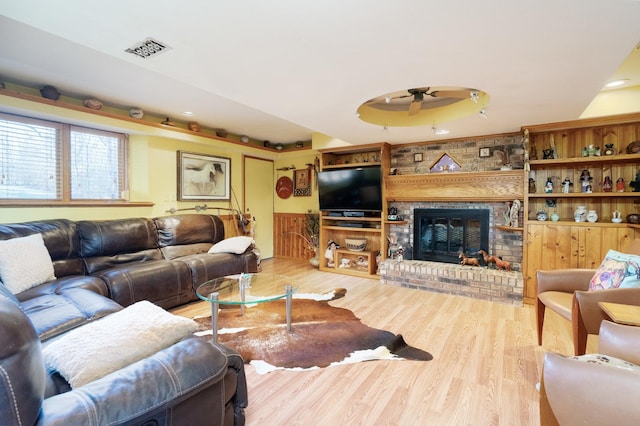 living room featuring ceiling fan, a fireplace, wood finished floors, and visible vents