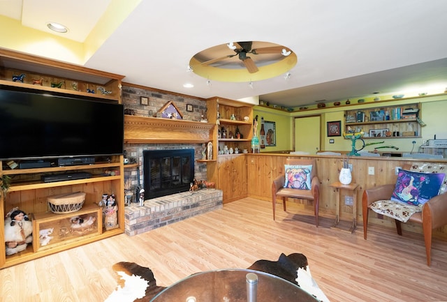 living area featuring a ceiling fan, light wood-type flooring, a raised ceiling, and a fireplace