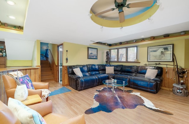 living room with light wood-style floors, a tray ceiling, wainscoting, and stairway