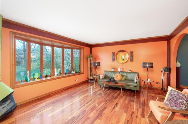 living area featuring arched walkways, ornamental molding, wood finished floors, and baseboards