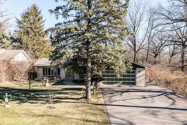 view of property hidden behind natural elements with driveway, a garage, a front lawn, and brick siding