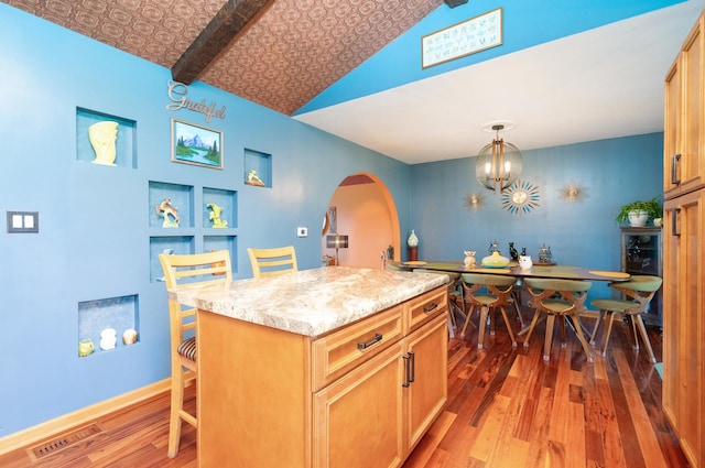 kitchen featuring visible vents, a breakfast bar, wood finished floors, decorative light fixtures, and a center island