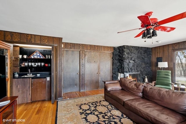 living room featuring a ceiling fan, wood finished floors, wet bar, wood walls, and a fireplace