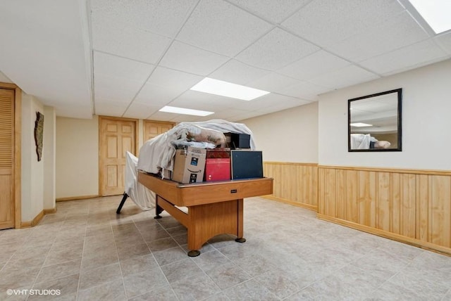 recreation room featuring a paneled ceiling, a wainscoted wall, and wooden walls