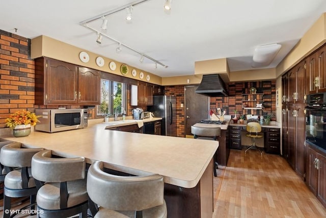 kitchen featuring light wood-type flooring, appliances with stainless steel finishes, light countertops, and exhaust hood