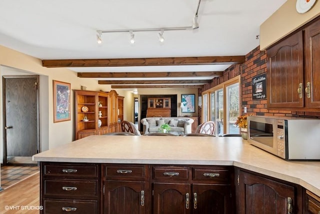 kitchen featuring light wood-style flooring, a peninsula, dark brown cabinets, light countertops, and stainless steel microwave