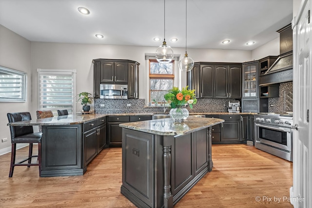 kitchen with a center island, a breakfast bar, light wood-type flooring, appliances with stainless steel finishes, and a peninsula