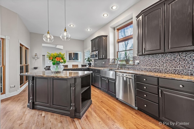 kitchen with a kitchen island, light wood-style flooring, a sink, appliances with stainless steel finishes, and tasteful backsplash