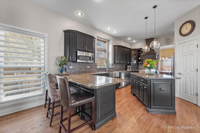 kitchen with stainless steel microwave, light wood-style floors, tasteful backsplash, and dark stone counters