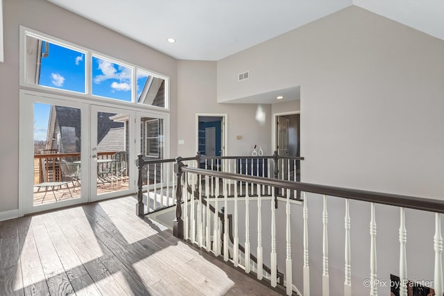 corridor with visible vents, an upstairs landing, french doors, wood finished floors, and high vaulted ceiling