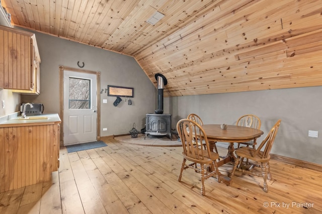 dining space with wood ceiling, light wood-type flooring, lofted ceiling, and a wood stove