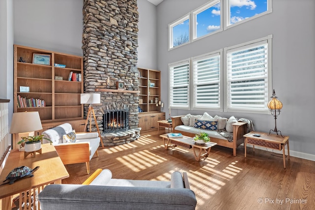 living area with a fireplace, a high ceiling, baseboards, and wood finished floors