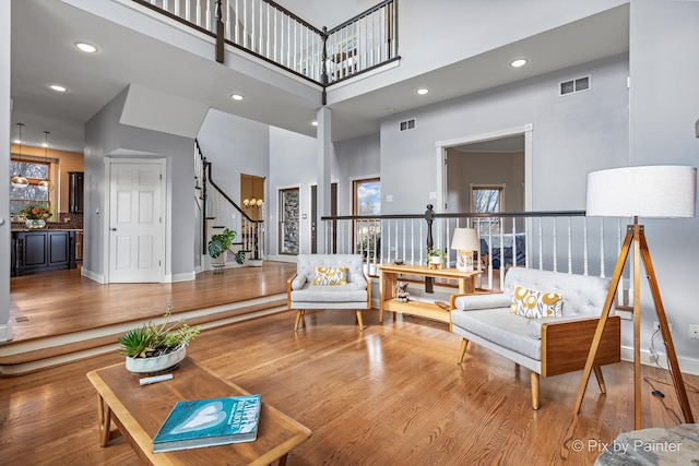 living area with visible vents, stairway, a towering ceiling, and wood finished floors