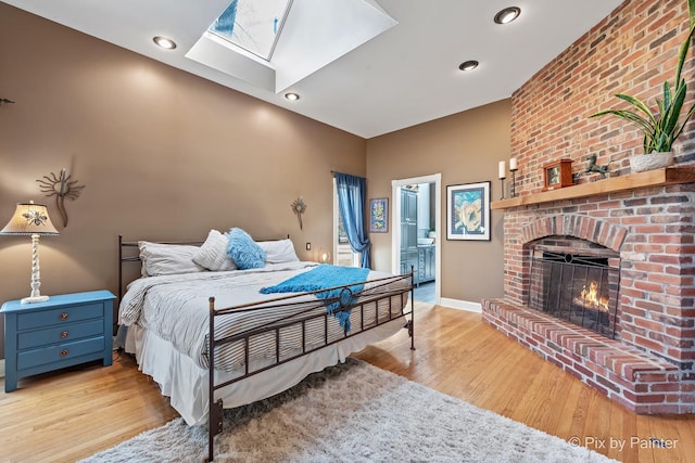 bedroom with baseboards, a skylight, a fireplace, and light wood finished floors