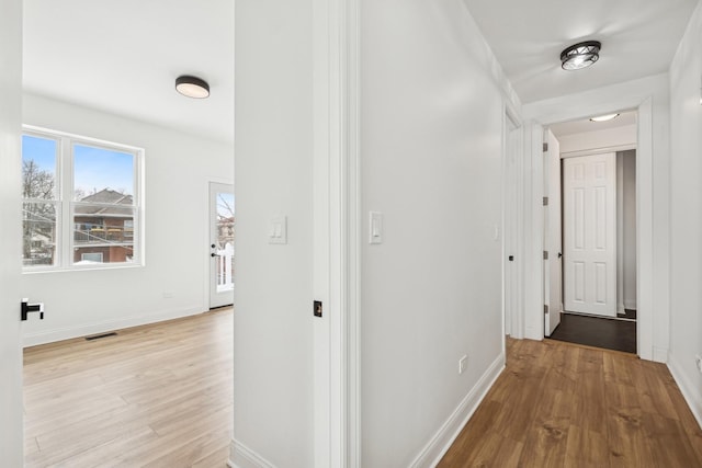 corridor with baseboards, visible vents, and light wood-style floors