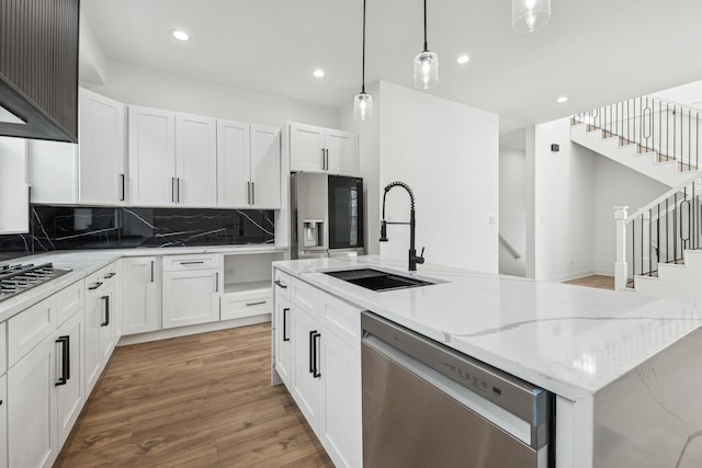 kitchen with a sink, white cabinetry, appliances with stainless steel finishes, light wood-type flooring, and an island with sink