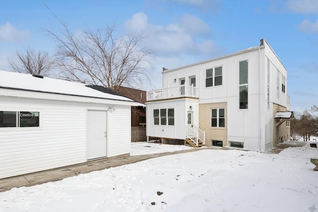 snow covered rear of property featuring a balcony, an outdoor structure, and entry steps