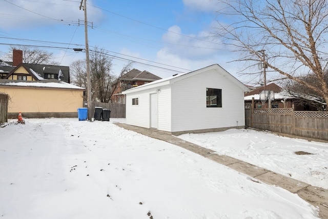 snow covered back of property with an outdoor structure, fence, and a detached garage