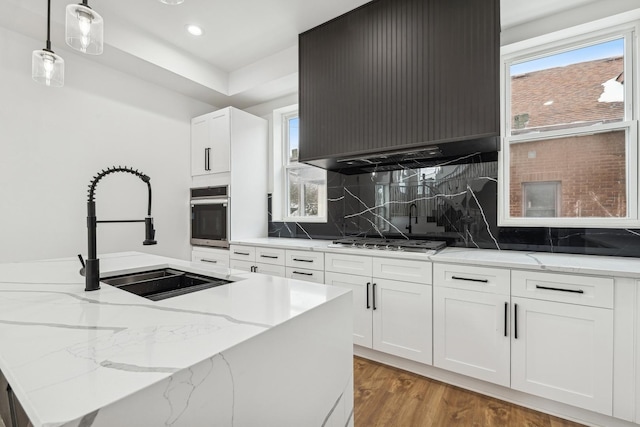 kitchen featuring custom exhaust hood, decorative backsplash, appliances with stainless steel finishes, light wood-style floors, and a sink