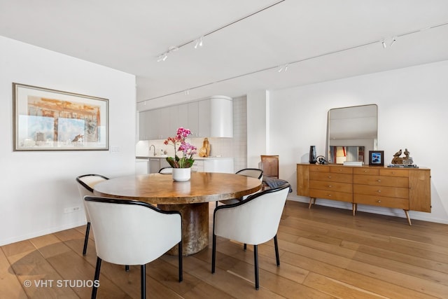 dining area featuring rail lighting, light wood-style flooring, and baseboards