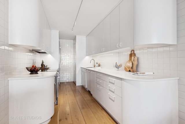 kitchen with a sink, light wood-style floors, white cabinets, light countertops, and appliances with stainless steel finishes