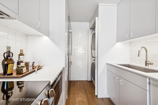 clothes washing area with laundry area, stacked washer and dryer, a sink, and light wood-style flooring