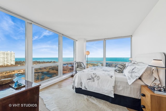 bedroom featuring expansive windows, a water view, and light wood-style floors