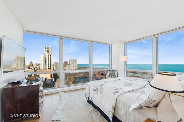 bedroom with expansive windows, a water view, and light wood-style floors