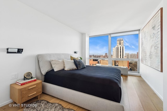 bedroom with a city view, baseboards, and wood finished floors