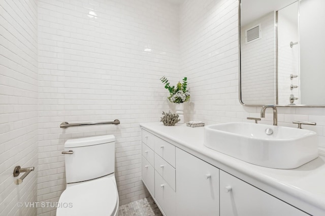 bathroom featuring toilet, visible vents, tile walls, and vanity