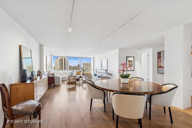 dining room with a city view, rail lighting, and light wood-style floors