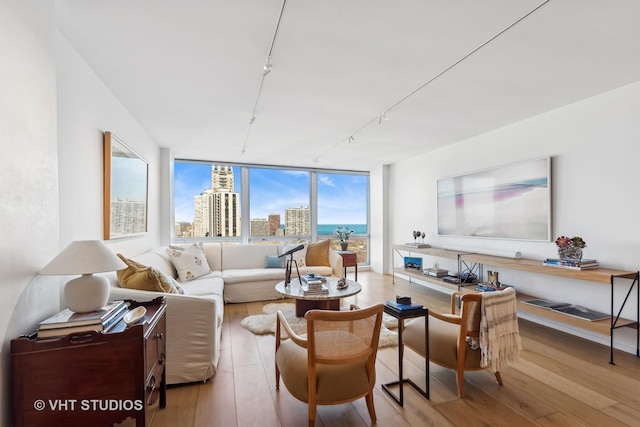 living area with a view of city, floor to ceiling windows, track lighting, and light wood-style floors