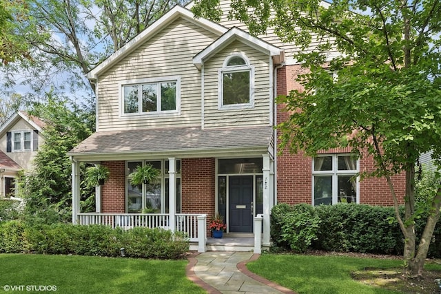 traditional-style home with covered porch, brick siding, a front yard, and a shingled roof