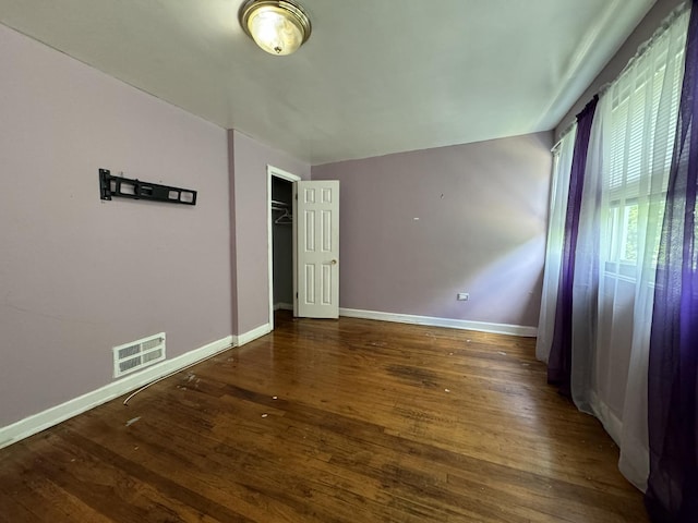 unfurnished bedroom with a closet, dark wood finished floors, visible vents, and baseboards