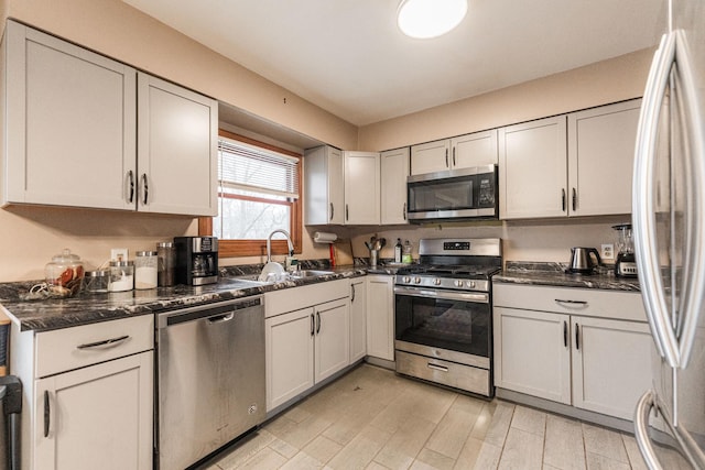 kitchen featuring dark stone counters, appliances with stainless steel finishes, a sink, and white cabinets