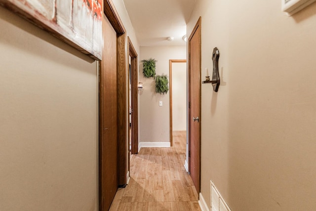 hall with light wood-type flooring, visible vents, and baseboards