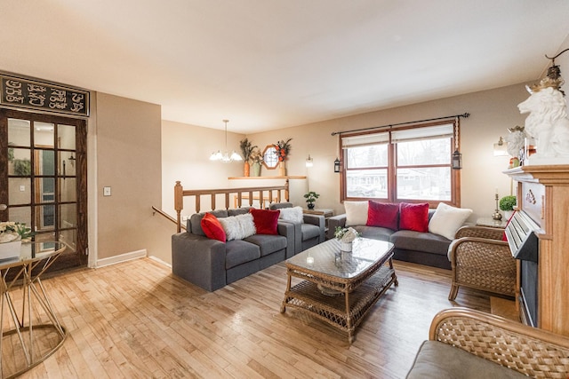 living room featuring a chandelier, a fireplace, light wood-style flooring, and baseboards