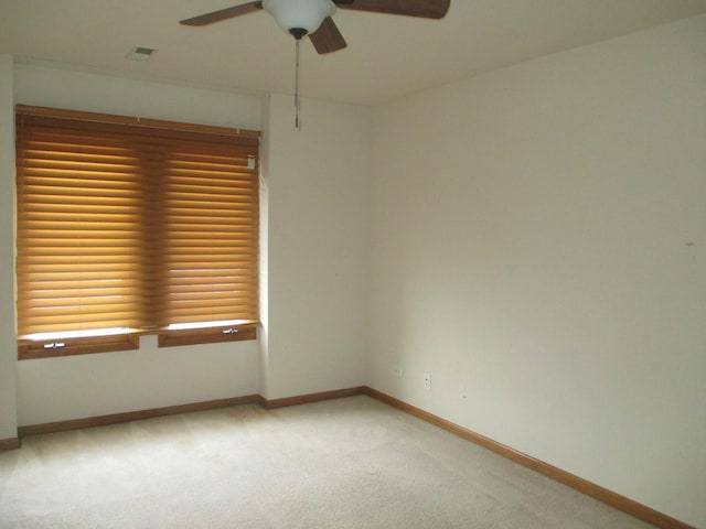 spare room featuring light colored carpet, ceiling fan, visible vents, and baseboards