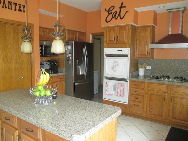 kitchen with white appliances, light tile patterned floors, wall chimney exhaust hood, brown cabinets, and light countertops