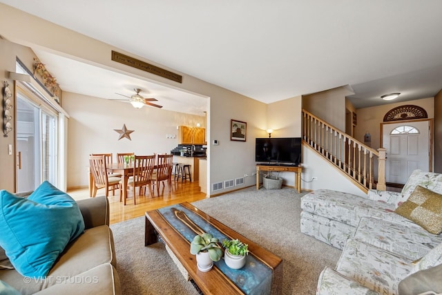 living area with visible vents, stairway, a ceiling fan, wood finished floors, and baseboards