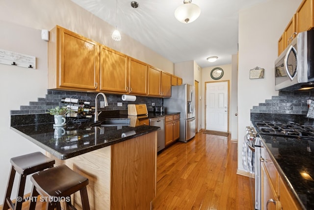 kitchen featuring a breakfast bar area, light wood-style flooring, a peninsula, a sink, and appliances with stainless steel finishes