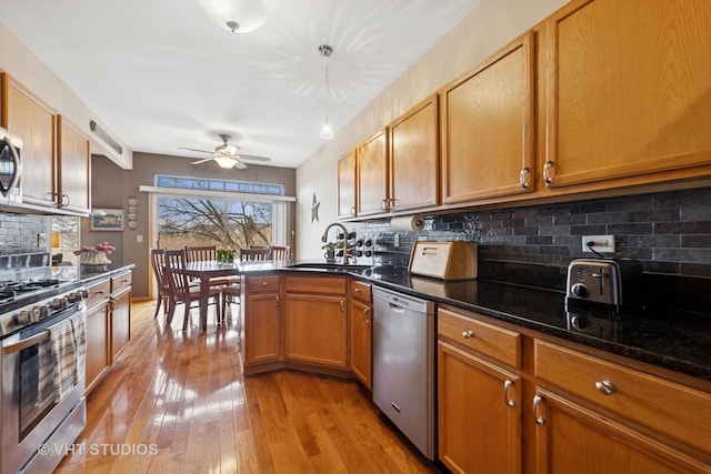 kitchen featuring brown cabinets, stainless steel appliances, light wood-style floors, a ceiling fan, and a sink