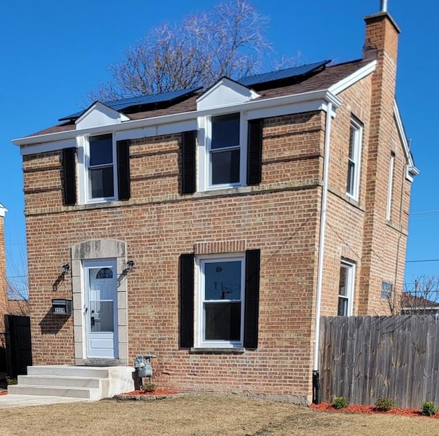 view of front facade with solar panels, brick siding, and fence